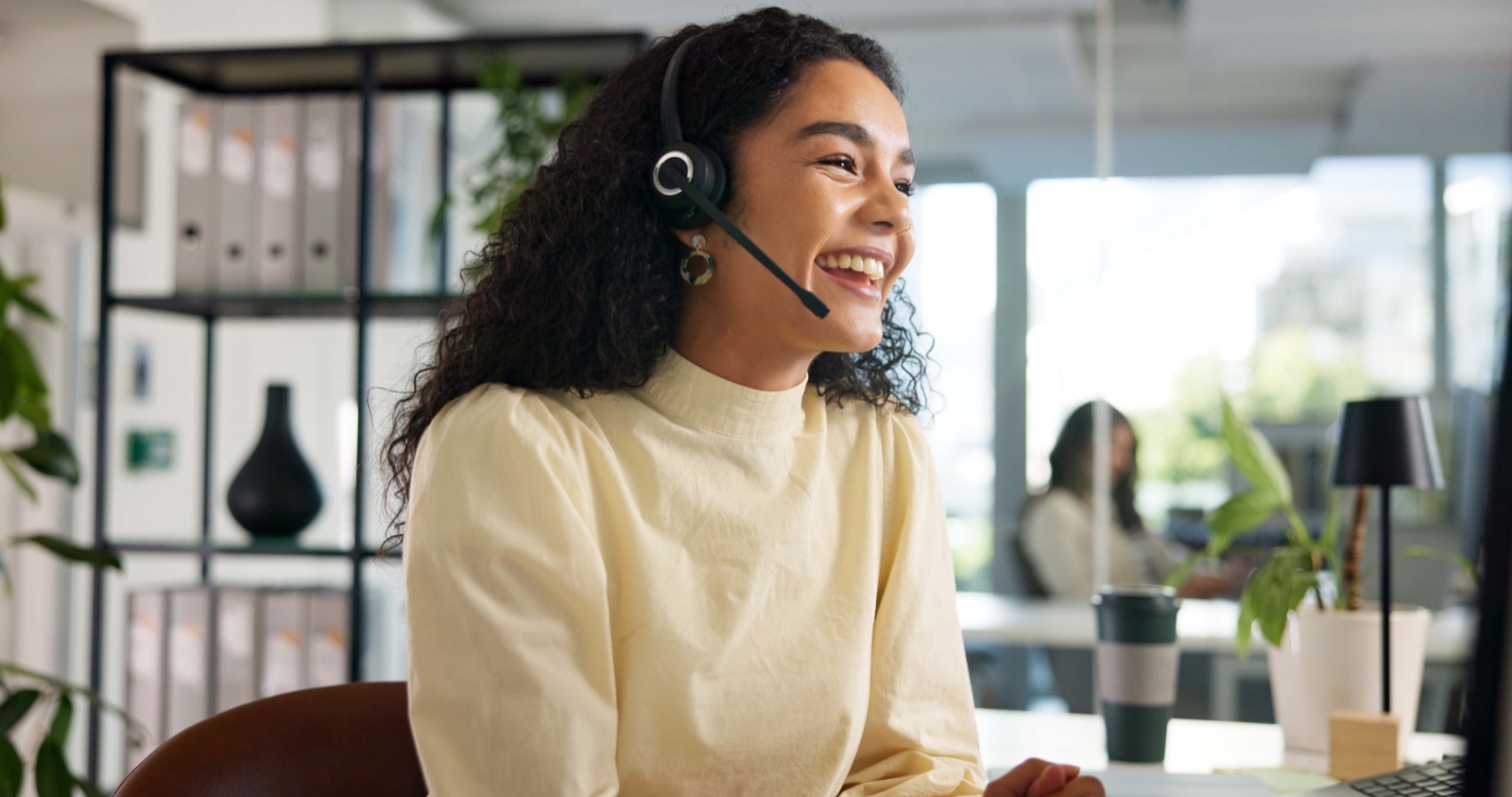 A customer service adviser on a headset, laughing during a call in a bright office